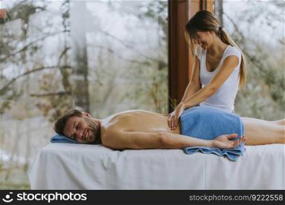 Handsome young man lying and having back massage in spa salon during winter season by the female masseur