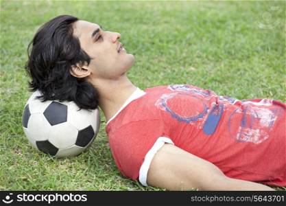 Handsome young man lying on back with head on soccer ball