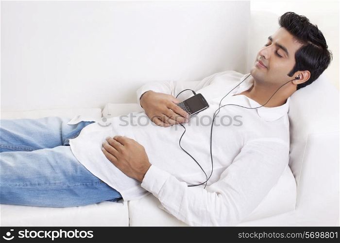 Handsome young man lying on sofa while listening to music
