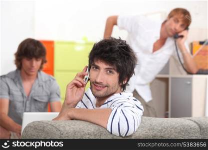 Handsome young man making a call with his friends doing the same in the background