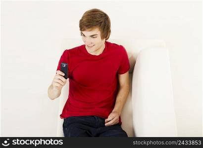 Handsome young man on the couch sending a text messages with cellphone