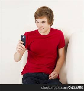 Handsome young man on the couch sending a text messages with cellphone
