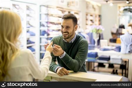 Handsome young man paying with a credit card in the clotging store