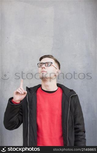 handsome young man pointing his finger upward looking up against concrete wall