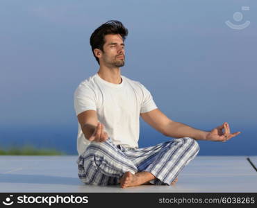 handsome young man practicing yoga on in modern home terace with ocean and sunset in background