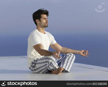 handsome young man practicing yoga on in modern home terace with ocean and sunset in background