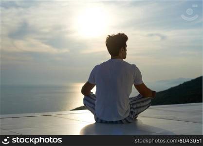 handsome young man practicing yoga on in modern home terace with ocean and sunset in background