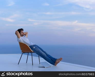 handsome young man relaxing and working on laptop computer at home balcony while looking sunset