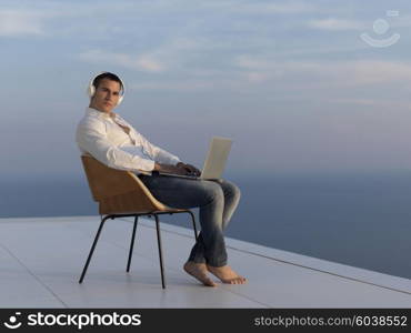 handsome young man relaxing and working on laptop computer at home balcony while looking sunset