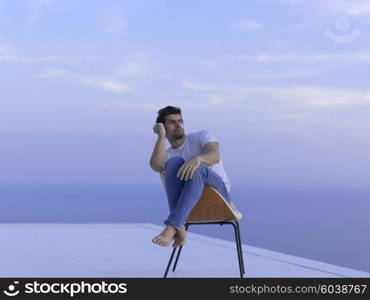 handsome young man relaxing and working on laptop computer at home balcony while looking sunset