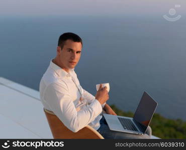 handsome young man relaxing and working on laptop computer at home balcony while looking sunset