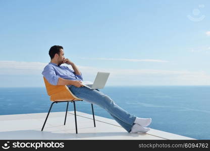 handsome young man relaxing and working on laptop computer at home balcony while looking sunset