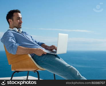 handsome young man relaxing and working on laptop computer at home balcony while looking sunset