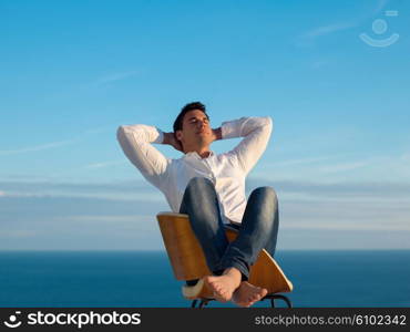 handsome young man relaxing and working on laptop computer at home balcony while looking sunset