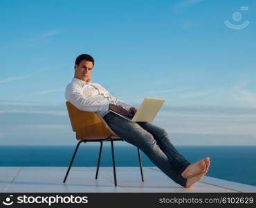 handsome young man relaxing and working on laptop computer at home balcony while looking sunset