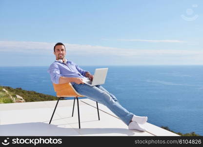 handsome young man relaxing and working on laptop computer at home balcony while looking sunset