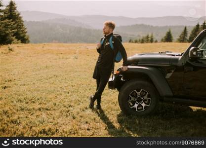 Handsome young man relaxing  by the terrain vehicle hood at countryside