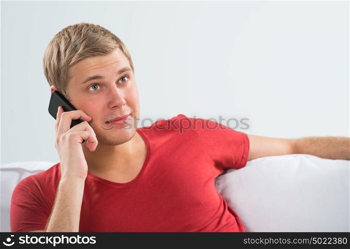 Handsome young man relaxing on sofa and calling with his smart phone