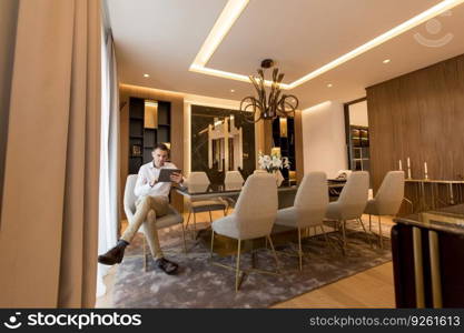 Handsome young man sitting and using digital tablet at luxury apartment