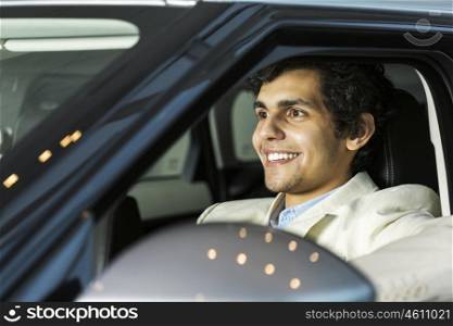Handsome young man sitting in car in showroom . Buying car
