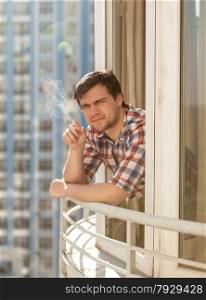 Handsome young man smoking cigarette on balcony