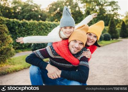 Handsome young man spends his free time with family, recieves embrace from adorable daughter and pretty wife, have picnic during autumn weekend. Happy affectionate family have good relationships.