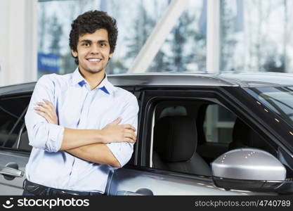 Handsome young man standing besides car in showroom . Buying car