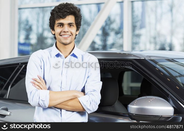 Handsome young man standing besides car in showroom . Buying car