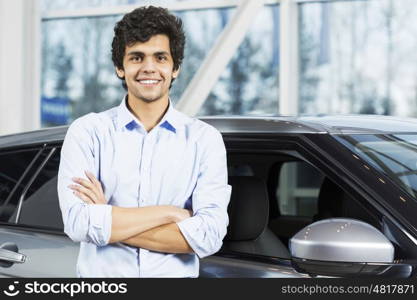 Handsome young man standing besides car in showroom . Buying car