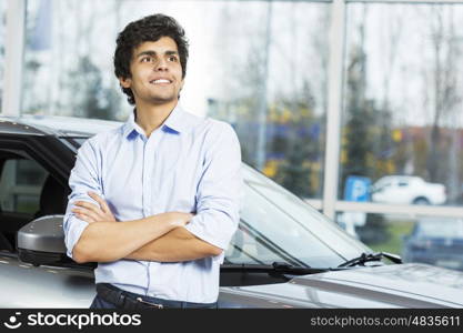 Handsome young man standing besides car in showroom . Buying car