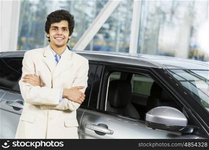 Handsome young man standing besides car in showroom . Buying car