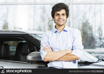 Handsome young man standing besides car in showroom . Buying car