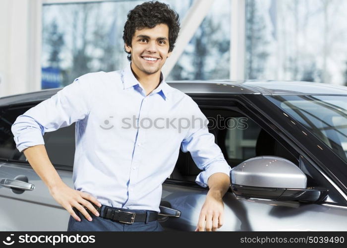 Handsome young man standing besides car in showroom . Buying car