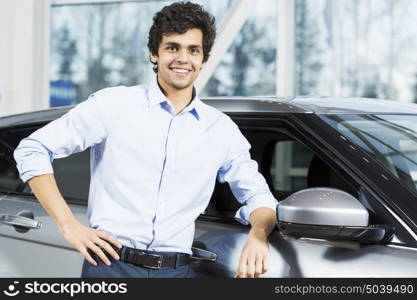 Handsome young man standing besides car in showroom . Buying car