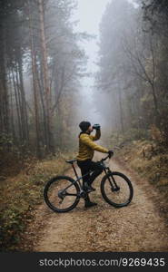 Handsome young man taking a brake during biking through autumn forest