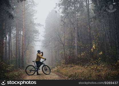 Handsome young man taking a brake during biking through autumn forest