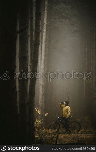 Handsome young man taking a brake during biking through autumn forest