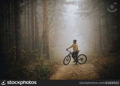 Handsome young man taking a brake during biking through autumn forest