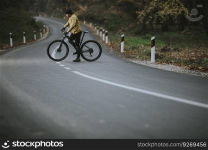 Handsome young man taking a brake on a country road during biking through autumn forest