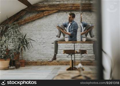 Handsome young man using digital tablet while sitting on the table in the rustic room