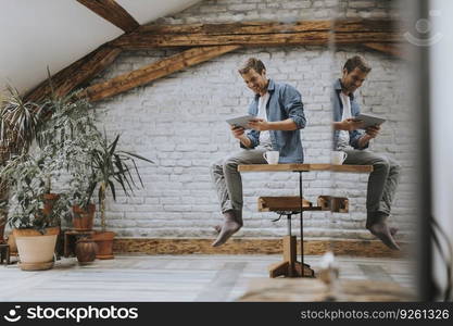 Handsome young man using digital tablet while sitting on the table in the rustic room