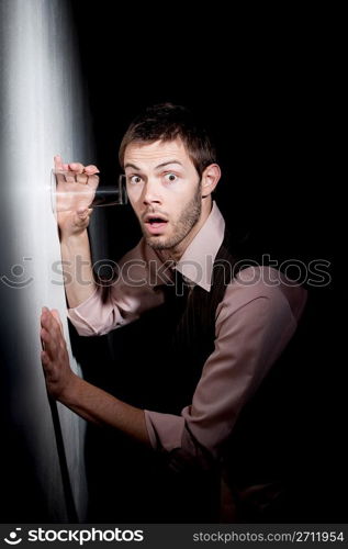 Handsome young man using glass to eavesdrop