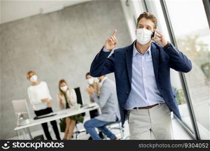 Handsome young man using mobile phone while wear protective masks to prevent corona viruus at office space