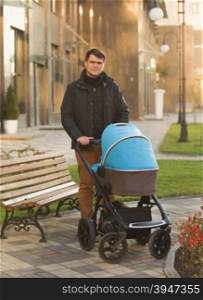 Handsome young man walking with baby in stroller on street