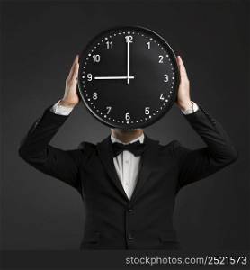 Handsome young man wearing a tuxedo and holding a clock