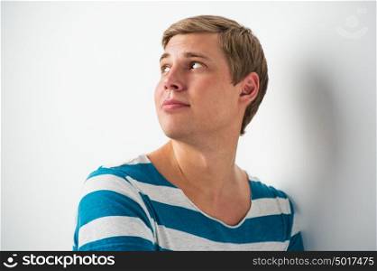 Handsome young man with a charming smile and look leaning on the wall and looking away