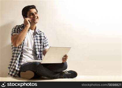 Handsome young man with laptop talking on cell phone