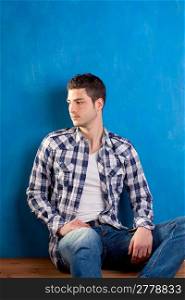 handsome young man with plaid shirt sitting on wood in blue background