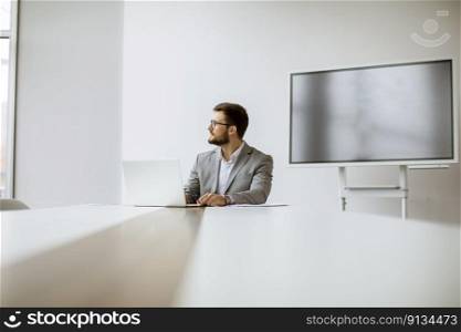 Handsome young man working on laptop in bright office with big screen behind him