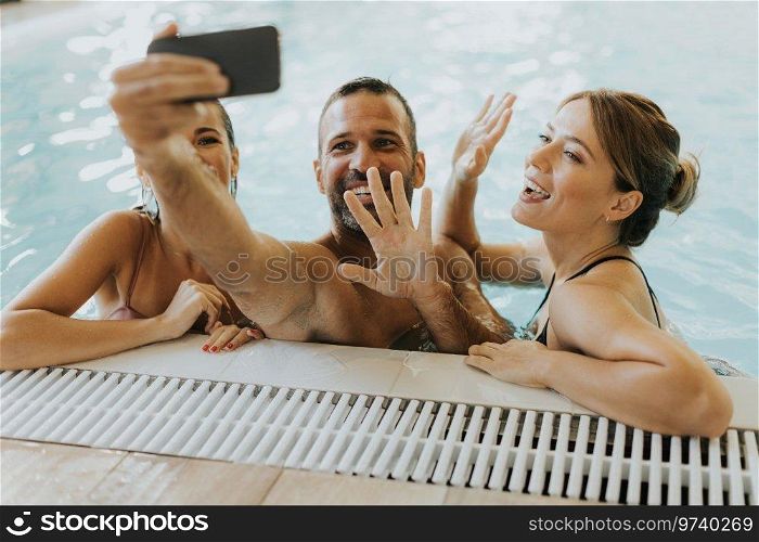 Handsome young people relaxing in the indoor swimming pool and taking selfie with mobile phone